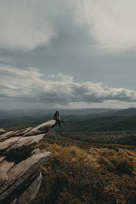 View of a man sitting on a rock in the mountains in North Carolina, the state where our BCBS drug rehab is located.