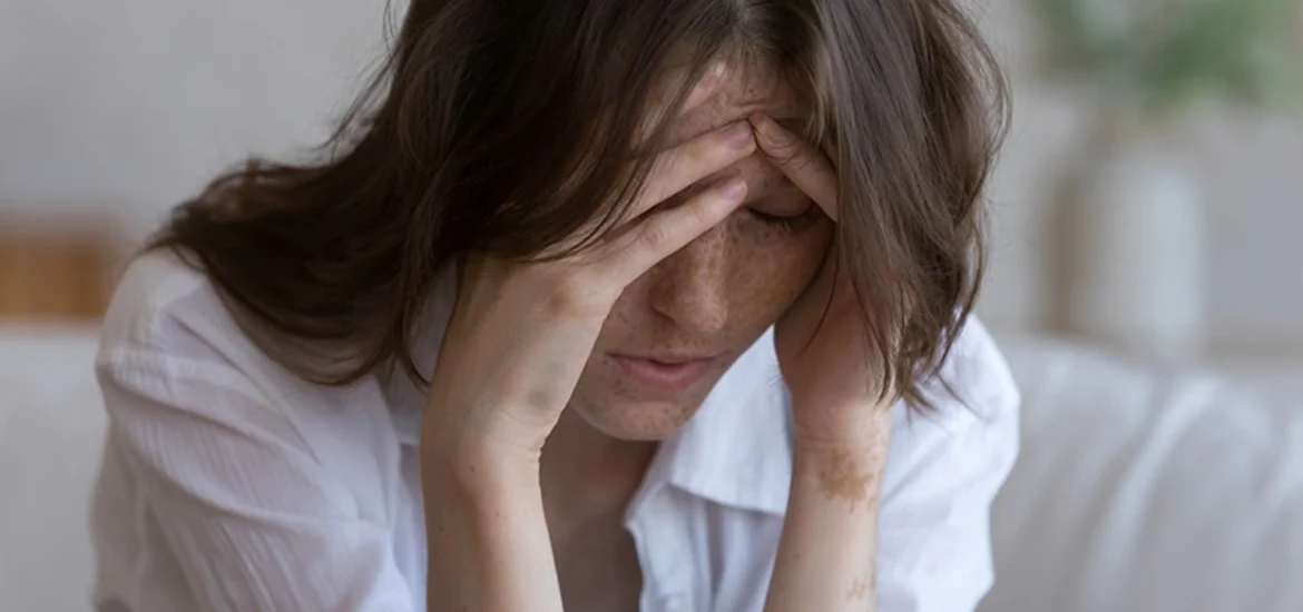 A woman who is struggling with chronic stress and substance abuse covers her face in distress.