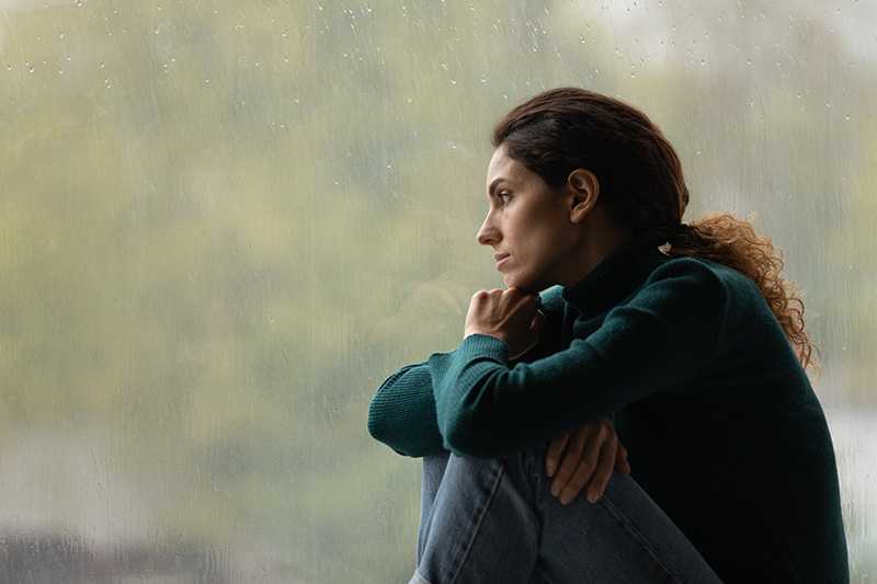 A woman struggling with PTSD sits by a window.